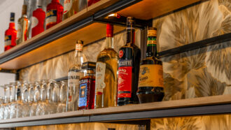 Eine gut bestückte Bar mit Spirituosenflaschen, Weingläsern und Likören im DIVINO in Hallbergmoos vor floralem Dekor.