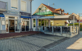 Straßenansicht des DIVINO in Hallbergmoos mit verglaster, überdachter Terrasse und sichtbarem Pizzeria-Bistrot-Eingang